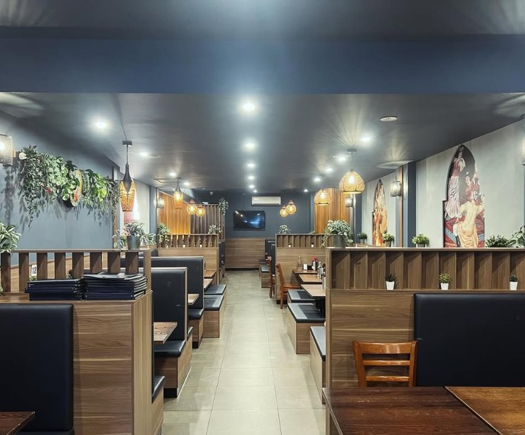 Long dining room aisle at Kaynam lined with wooden booths, plants and glowing lanterns