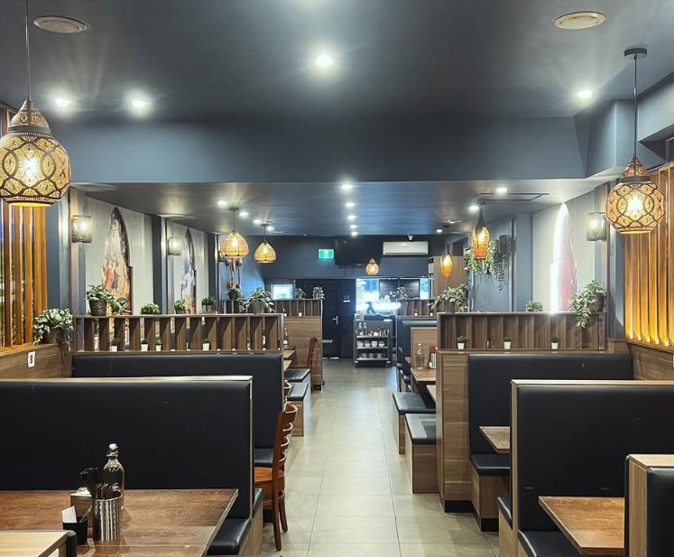 View down the main dining room aisle past booths and brass lanterns toward the kitchen